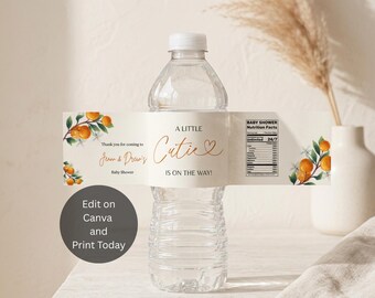 May include: A clear plastic water bottle with a rectangular paper label featuring orange fruit illustrations, green leaves, and the text A LITTLE Cutie IS ON THE WAY! along with Jenna & Drew's Baby Shower and a nutrition facts panel.