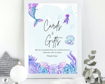 May include: A white sign with a blue and purple mermaid, jellyfish, and seashells. The sign says "Cards & Gifts" and "We are so grateful that you could be here to celebrate with us today! Thank You!"