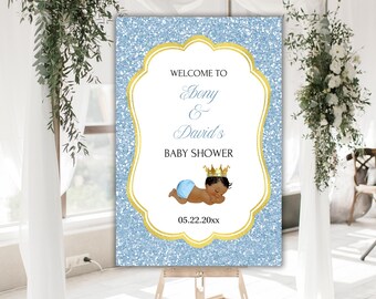 May include: Welcome to Bony & David's Baby Shower sign with a blue glitter background and gold trim. The sign features a cartoon illustration of a baby boy wearing a crown and sleeping. The date 05.22.20xx is printed below the illustration.