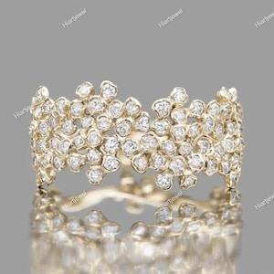 Könnte beinhalten: Ein goldfarbener Ring mit floralem Design, besetzt mit zahlreichen kleinen, funkelnden Diamanten. Das detaillierte Muster des Rings spiegelt sich in der darunter liegenden Oberfläche wider und erzeugt ein symmetrisches Bild. Der Ring ist ein Schmuckstück.