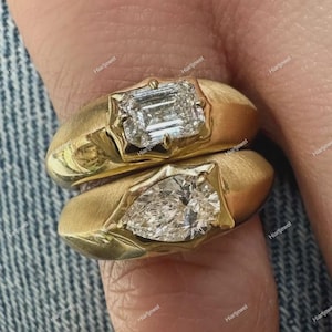 Peut inclure: Deux bagues en or avec une finition mate, chacune ornée d'une pierre précieuse transparente. La bague supérieure porte une pierre rectangulaire taille émeraude, tandis que la bague inférieure présente une pierre en forme de poire.