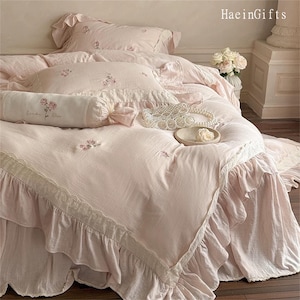 May include: A pink ruffled bedspread with delicate lace trim and floral embroidery. The bedspread is made of soft, lightweight fabric and features a ruffled design around the edges.