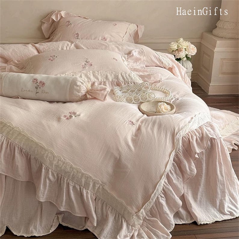 May include: A pink ruffled bedspread with delicate lace trim and floral embroidery. The bedspread is made of soft, lightweight fabric and features a ruffled design around the edges.