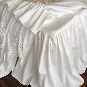 May include: White bedding set with ruffled edges and a lace detail. A book and a tube of hand cream rest on the bed. The bedding has a smooth, satin-like texture, creating a luxurious look. The brand name "HaeinGifts" is visible in the top right corner.