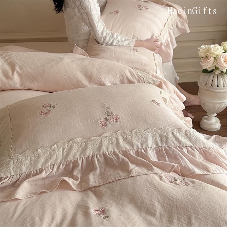 May include: A pink and white bedding set with a ruffled edge and floral embroidery. The bedding is made of a soft, comfortable fabric and features a delicate lace trim.