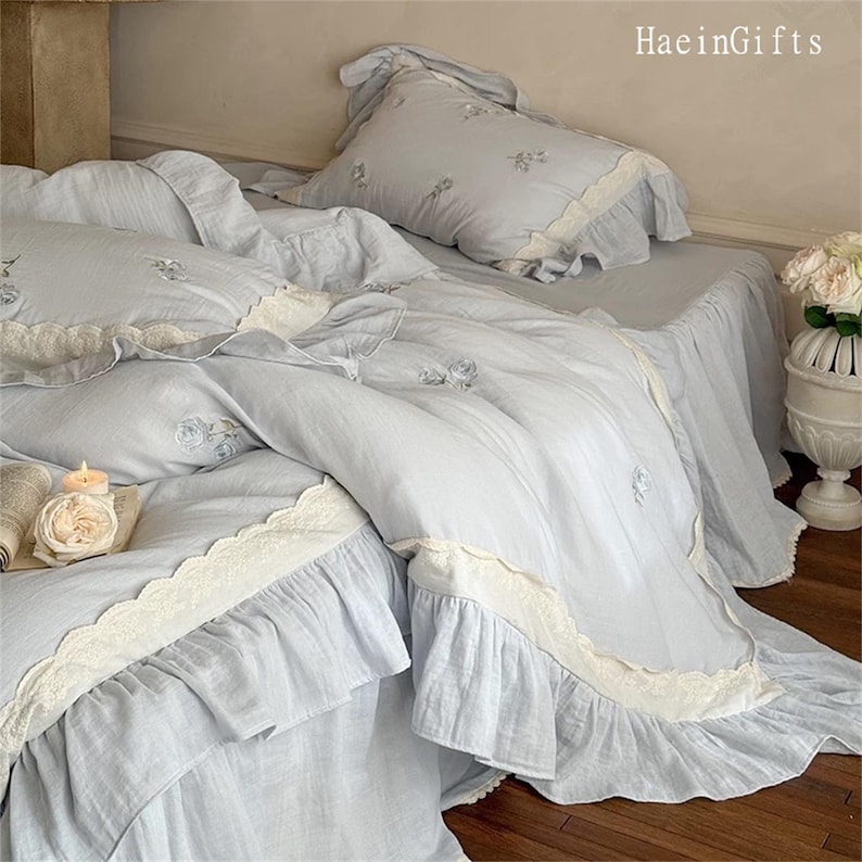 May include: A light blue bed set with a white lace trim and floral embroidery. The bedding features a ruffled design and a matching pillow with a lace trim.