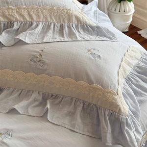 May include: A light blue bedspread with a white lace trim and embroidered floral designs. The bedspread has a ruffled edge and is made of a soft, comfortable fabric.