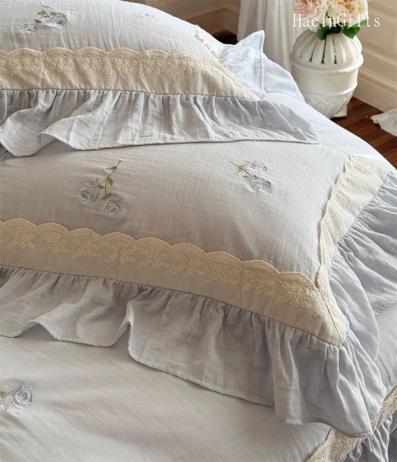 May include: A light blue bedspread with a white lace trim and embroidered floral designs. The bedspread has a ruffled edge and is made of a soft, comfortable fabric.