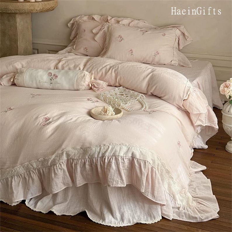 May include: A pink ruffled bedspread with a white lace trim and embroidered floral details. The bedspread is made of a soft, lightweight fabric and is perfect for adding a touch of elegance to any bedroom.