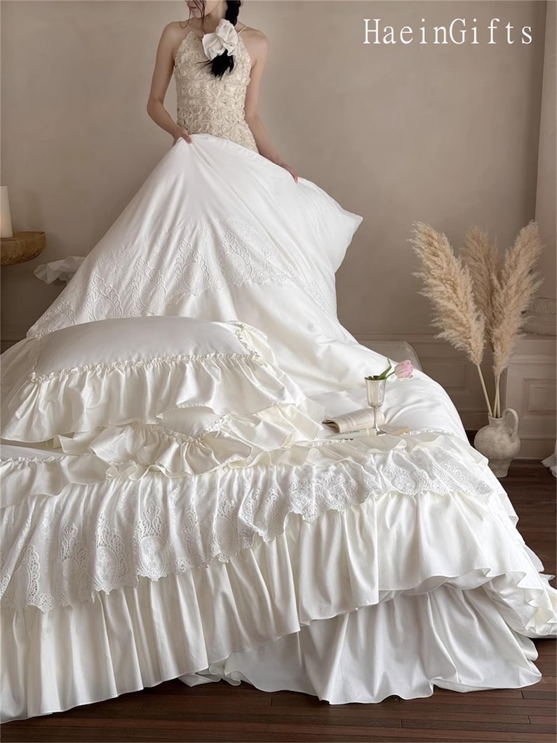 May include: Ivory-colored bedding set with ruffled edges and lace detailing. The set includes a comforter, pillow, and bed skirt. The image also shows a person holding the comforter. The text "HaeinGifts" is visible in the upper right corner.