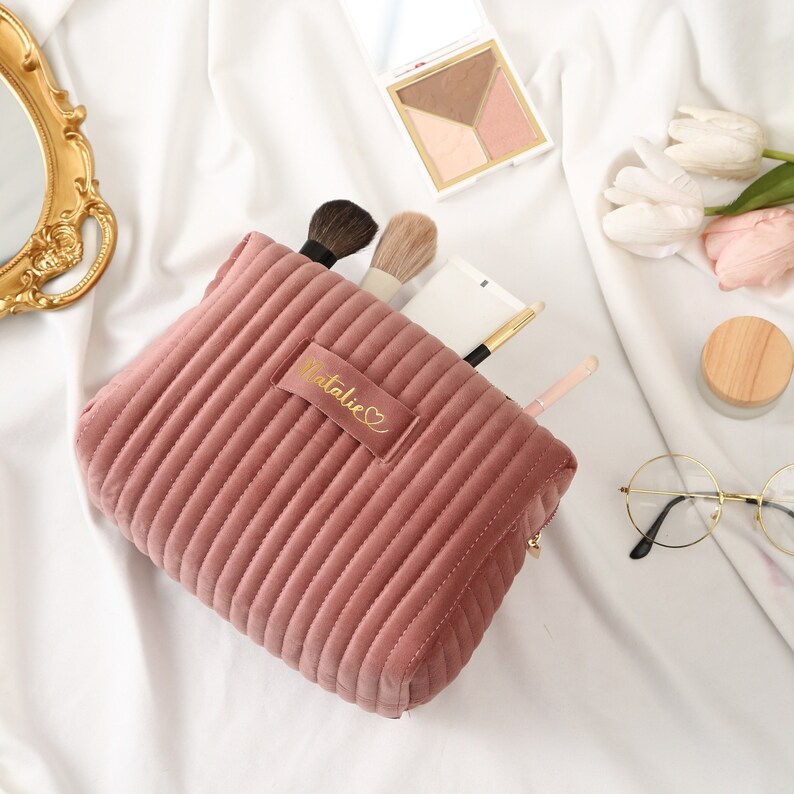 a pink purse sitting on top of a bed next to a mirror