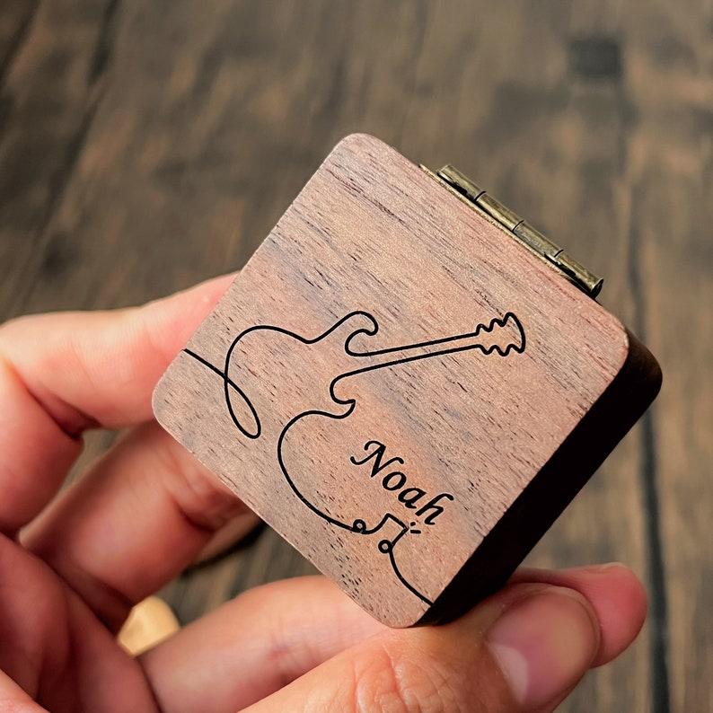 a person holding a wooden lighter case with a drawing of a guitar on it