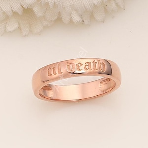 May include: Rose gold ring with the inscription "til death" in an elegant, gothic-style font. The ring has a smooth, polished finish and a classic band design. The ring is a symbol of commitment and love.