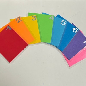 May include: A set of eight colorful cards with numbers 1 through 8 printed on them. The cards are arranged in a rainbow pattern, with red, orange, yellow, green, blue, purple, pink, and white.