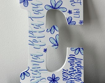 May include: A white wooden letter E decorated with hand-painted blue flowers in various shades. The text Sigma Delta Tau is written vertically, with est. 1917 and Indiana University 2026 printed in blue script on the surface of the letter.