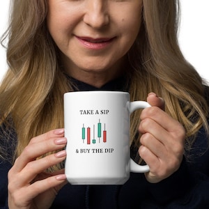 Puede incluir: Taza de cerámica blanca con asa negra. La taza tiene un gráfico negro y verde de un gráfico de mercado de valores con el texto "Take a Sip & Buy the Dip".