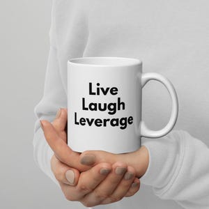 May include: White ceramic coffee mug with black text that reads "Live Laugh Leverage".