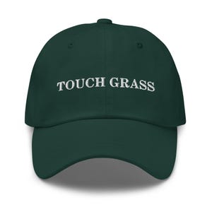 Könnte beinhalten: Eine dunkelgrüne Baseballkappe mit weiß gesticktem Text, der "TOUCH GRASS" lautet.