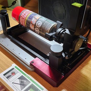 Puede incluir: Una lata roja y plateada etiquetada "ACCELERATE" se sostiene en una máquina negra y plateada. La máquina tiene una base roja y una serie de engranajes y palancas. Se ve una tarjeta con instrucciones.