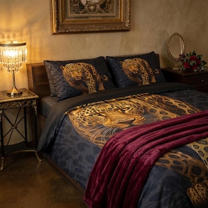 May include: A bedding set featuring a dark gray background with a large, detailed leopard print pattern on the duvet cover and two matching pillowcases. A solid, deep burgundy velvet-textured throw blanket is draped across the foot of the bed.