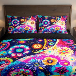 Puede incluir: Un vibrante juego de cama con un colorido diseño de cachemir y flores. La ropa de cama incluye dos fundas de almohada y una funda nórdica, que muestra una mezcla de tonos azules, rosas, amarillos y morados. La cama está hecha con una sábana negra.