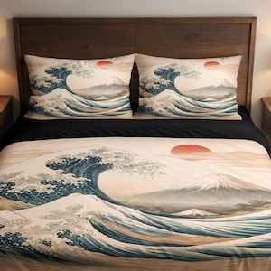 Op de afbeelding: Beddengoedset met een Japans geïnspireerd ontwerp met een grote golf, een rode zon en een berg op de achtergrond. De set bevat een dekbedovertrek en twee kussenslopen, allemaal met dezelfde print. Het kleurenpalet omvat blauw, beige en rood.