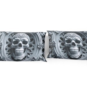 May include: Two decorative pillowcases with a detailed skull design. The skull is set within an ornate, circular frame with floral accents. The color palette is grayscale, with varying shades of gray.