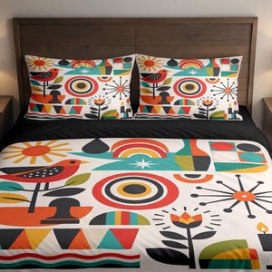 Könnte beinhalten: Ein Bett mit einer Bettdecke und zwei passenden Kissenbezügen. Die Bettwäsche zeigt ein farbenfrohes geometrisches Design mit Vögeln, Sonnen und floralen Elementen in Rot, Orange, Türkis und Schwarz auf weißem Hintergrund. Das Bett ist mit einem schwarzen Laken bezogen.