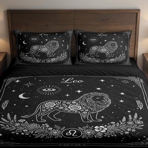 May include: Black bedding set featuring a detailed white illustration of a lion, surrounded by floral and celestial elements. The word "Leo" is displayed on the duvet cover and pillowcases. The set includes a duvet cover and two pillowcases.