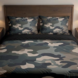 Peut inclure: Ensemble de literie à motif camouflage, comprenant une housse de couette et deux taies d'oreiller. Le motif utilise des tons de vert, de gris et de beige dans un imprimé d'inspiration militaire. Le lit est dans une chambre avec des meubles en bois et des lampes.