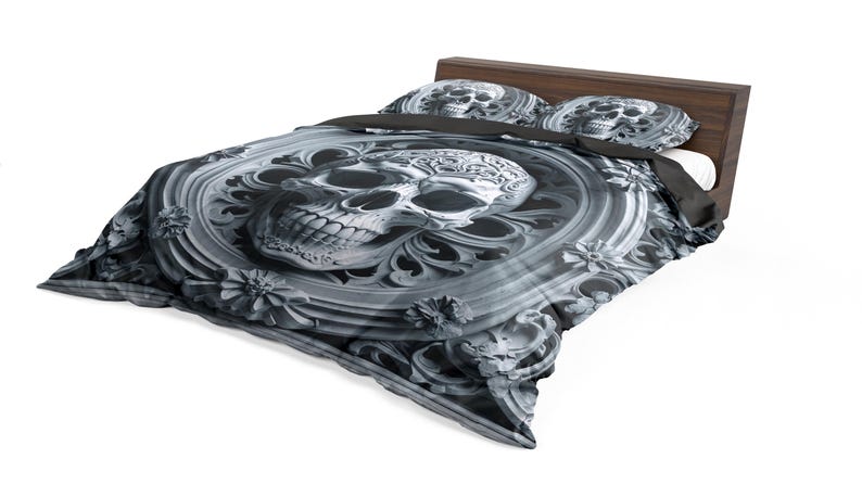 May include: A bed with a dark wooden headboard and a gray and white skull-themed bedding set. The duvet cover and pillowcases feature a detailed skull design within an ornate, floral-like frame. The overall aesthetic is gothic.