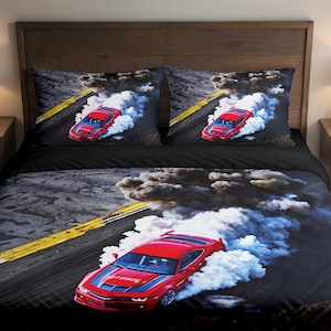 Könnte beinhalten: Schwarzes Bettwäsche-Set mit einem roten Sportwagen, der auf einer Rennstrecke driftet und weißen Rauch erzeugt. Das Set besteht aus einem Bettbezug und zwei Kissenbezügen. Das Rennmotiv zeigt einen gelb-weißen Streifen auf der Strecke.