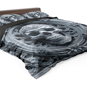 May include: A bed with a dark wooden frame and a skull-themed bedding set. The comforter and pillowcases feature a detailed, grayscale skull design with floral accents, creating a gothic aesthetic. The bedspread is a dark gray color.