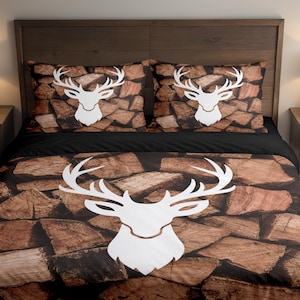 Könnte beinhalten: Bettwäsche-Set mit einem weißen Hirschkopf-Design auf einem Hintergrund aus gestapelten Holzscheiten. Das Set enthält einen Bettbezug und zwei Kissenbezüge. Die Farbgebung ist hauptsächlich Braun, Schwarz und Weiß.