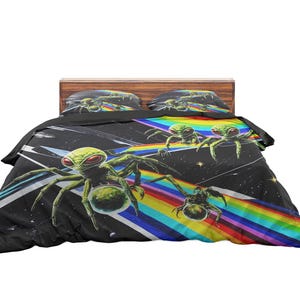 May include: A black and colorful bed set featuring a unique design. The bedding includes a comforter and two pillowcases. The design features green alien-like spiders, a rainbow, and a starry background. The bed set is placed on a wooden bed frame.