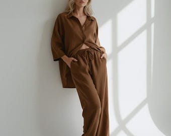 May include: A brown two-piece set consisting of a long-sleeved button-down shirt with a collar and matching wide-leg trousers. The trousers feature an elasticized waistband with a drawstring tie and side pockets, creating a coordinated outfit.