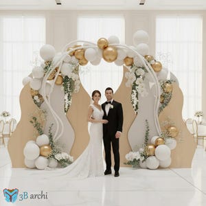 Könnte beinhalten: Eine Hochzeitsszene mit einem Paar vor einem dekorativen Bogen. Der Bogen ist mit weißen und goldenen Luftballons, weißen Blumen und Grün geschmückt. Der Hintergrund umfasst beige Tafeln mit einem wellenförmigen Design. Die Braut trägt ein weißes Spitzenkleid, der Bräutigam einen schwarzen Smoking.