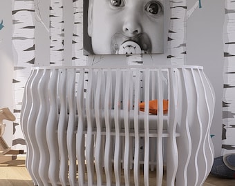 May include: White, modern crib with a unique wavy design. The crib has vertical slats and a curved shape. An orange pillow rests on the gray mattress inside. A black and white baby portrait hangs on the wall above the crib.