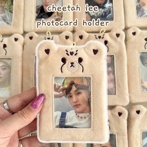 Op de afbeelding: Een beige fotokaarthouder met een berengezichtontwerp, met een foto van een persoon. De tekst "cheetah lee photocard holder" en "ver 2.0" zijn zichtbaar. De houder is omringd door vergelijkbare houders.