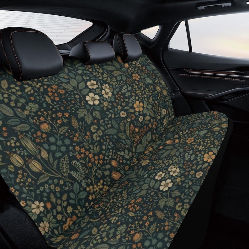 May include: Dark green car seat cover with a floral pattern featuring white, orange, and yellow flowers, along with green leaves and stems. The cover is designed to fit the back seat of a vehicle.