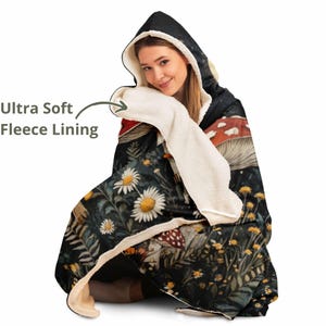 Puede incluir: Una manta con capucha de fondo negro y un dise&ntilde;o floral y de setas colorido. La manta tiene un forro de felpa suave y es perfecta para acurrucarse en el sof&aacute;.