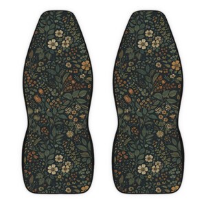 May include: Two car seat covers with a dark background and a floral pattern. The pattern includes various flowers and leaves in shades of cream, orange, and green. The covers have a black border and a contoured shape.