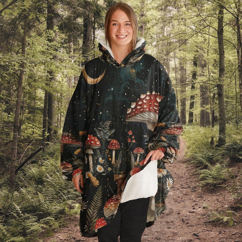 Puede incluir: Una manta con capucha de fondo azul oscuro y un dise&ntilde;o caprichoso con setas, estrellas y una luna creciente. La manta est&aacute; hecha de tela suave y mullida y tiene un forro de sherpa blanco.