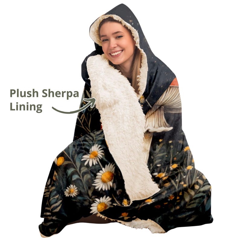 Puede incluir: Una manta con capucha con forro de sherpa suave. La manta presenta un fondo oscuro con un patr&oacute;n floral y una ilustraci&oacute;n de hongo.