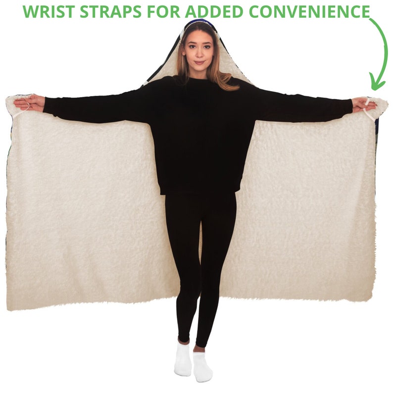 May include: A hooded blanket with a cream-colored, fluffy interior and a dark blue exterior trim. The blanket has wrist straps for added convenience. The person in the image is wearing a black sweater and black leggings.