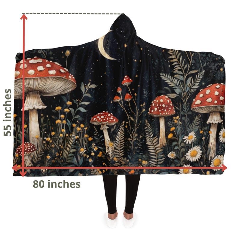 Puede incluir: Una manta con capucha que presenta una escena de bosque caprichosa con setas rojas y blancas, follaje verde y una luna creciente contra un cielo nocturno estrellado azul oscuro. La manta mide 140 cm por 203 cm.