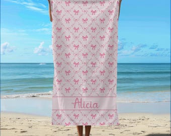 May include: A pink beach towel with a white background and a pattern of pink bows. The towel has the name "Alicia" printed on it in pink.