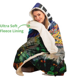 May include: A hooded blanket with an abstract design featuring a variety of colors, including green, blue, and yellow. The hood has a striped pattern in black and white. The blanket has an ultra-soft fleece lining.