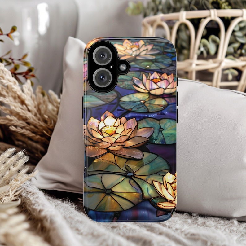 May include: A phone case with a stained glass design featuring water lilies in shades of yellow, white, and blue. The case has a black background and a camera lens cutout.