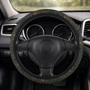 May include: A black steering wheel with a floral patterned cover. The cover features a dark green background with small yellow and blue flower designs. The steering wheel is in a car interior.